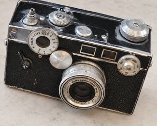 Vintage rangefinder film camera with silver-tone manual dials, an attached lens, and a black textured body with visible age and wear.