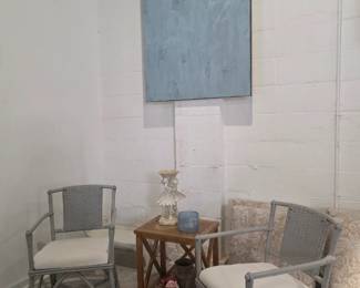 2 gray wicker chairs and end table with decor and wall art