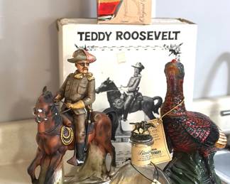 Collectible liquor bottles and decanters, including Theodore “Teddy” Roosevelt on horseback, a Wild Turkey ceramic turkey decanter, and an empty Blanton’s bourbon bottle