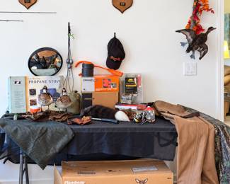 Assortment of hunting and outdoor gear, including mounted deer antlers, waterfowl taxidermy, fishing rods, a boxed propane stove, insulated waders with boots, and a boxed Flambeau Redi-Doe full-body deer decoy.