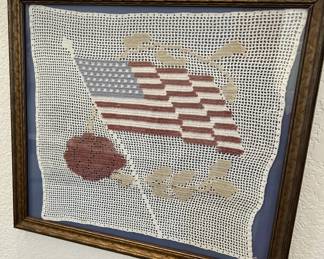 Framed vintage crochet lace piece featuring an American flag, rose, and leaf motifs, mounted on a blue background in a carved wooden frame.