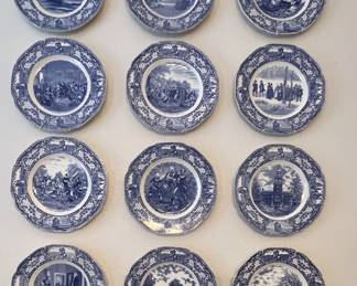 Collection of twelve vintage blue and white transferware plates, each featuring a different historical American scene with an ornate patterned border.