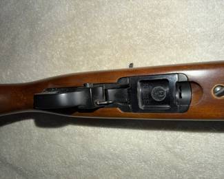 Close-up view of a Ruger rifle's underside, showing the wood stock, trigger guard, and the Ruger logo on the magazine release area.