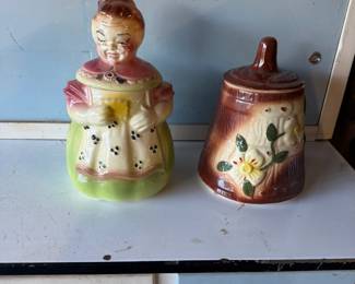 Vintage ceramic cookie jars, including a classic grandmother figure in an apron and a brown barrel-style jar with a raised floral motif.