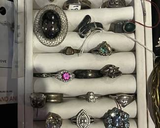 Assortment of vintage and modern rings displayed in a white jewelry tray, featuring various gemstones, metals, and designs.