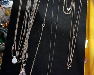 Assortment of fine silver and gold-tone chain necklaces, including two with teardrop-shaped gemstone pendants, displayed on a black velvet jewelry stand.