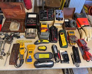 Assortment of vintage and modern electrical testing equipment, including multimeters, clamp meters, and various hand tools.
