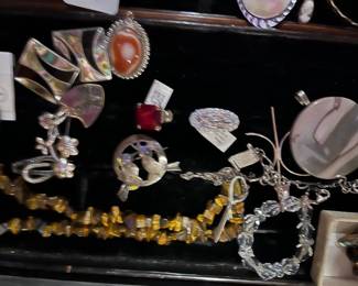 Assortment of vintage costume jewelry, including a tiger's eye chip necklace, silver-tone brooches, a red gemstone ring, and various pendants.