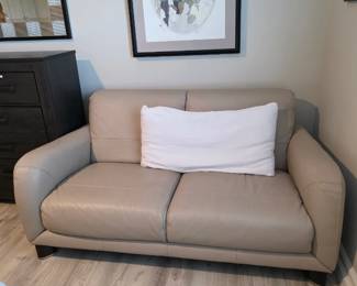 Taupe leather loveseat with track arms and white lumbar pillow