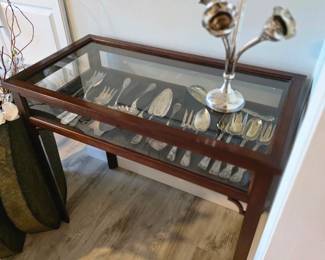 Mahogany-finish glass-top curio table with silver-tone flatware and ladles