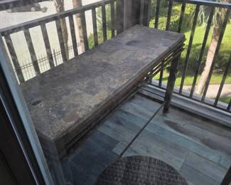 Slate-top outdoor bench on wicker base with round woven outdoor rug