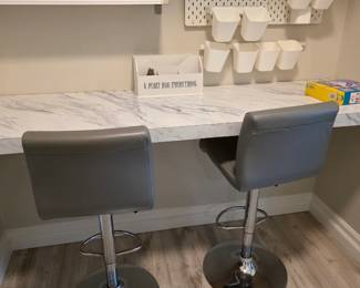 Gray faux leather counter stools with white pegboard bins and wall sign