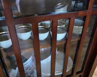 Dark wood glass-front china cabinet with gold-rim cups and floral china