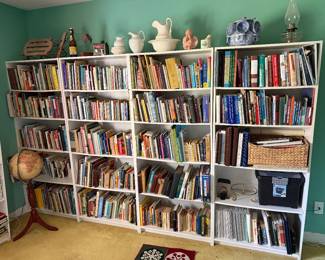 Wall of white bookcases filled with books, topped with ironstone pitcher and bowl sets, an oil lamp and a floor globe