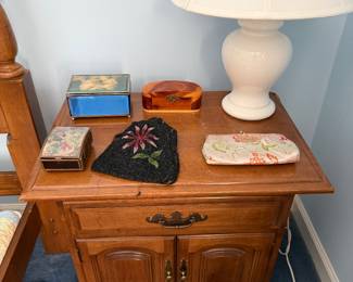 Nightstand with a white ceramic lamp, trinket boxes, a beaded purse and a brocade clutch