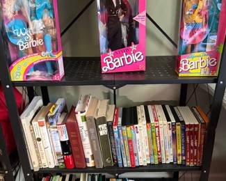 Boxed vintage Barbie dolls with shelves of books and VHS tapes