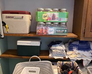 Pantry closet with Coleman coolers, boxed Ball mason jars, kitchen towels and storage baskets