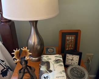 Nightstand with a brushed nickel lamp, antlered figure sculpture, vintage alarm clock and a pressed glass lidded dish