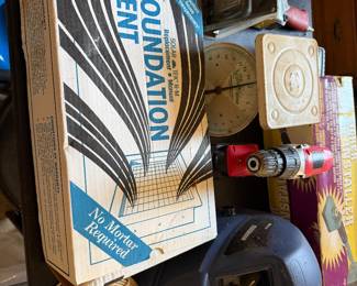 Boxed foundation vent, a cordless drill, a welding helmet and coiled wire