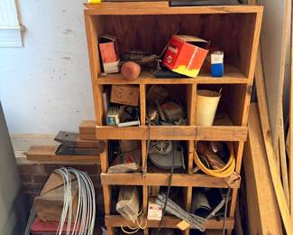 Wooden cubby shelving filled with hardware, electrical parts and coiled wire, with an antique sled above