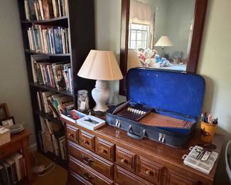 Wood dresser with attached mirror, table lamp and a bookcase of books