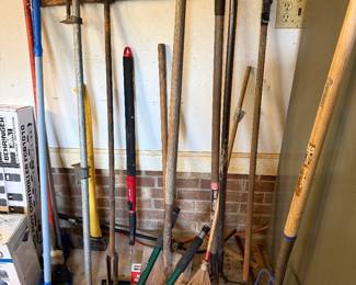 Long handled yard tools including rakes, shovels, loppers, a pitchfork and bar clamps