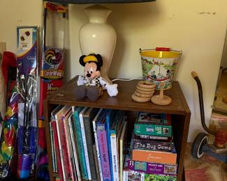 Bookcase of children's books and jigsaw puzzles with a table lamp, vintage tin sand pail and ring stacker