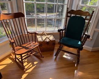 Two wooden rocking chairs, one stencil decorated with cushions, and a wicker picnic basket