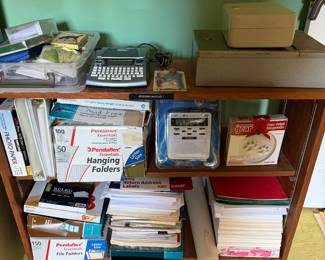 Shelf of office supplies including hanging file folders, paper, labels and a calculator