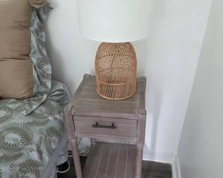Weathered wood nightstand with slatted lower shelf and rattan lamp