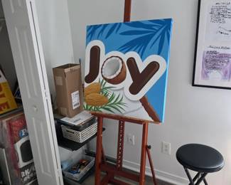 Pop art-style JOY canvas with coconut on wood studio easel and stool