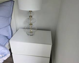 White two-drawer nightstand with stacked glass and brass table lamp