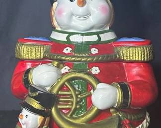 Toy Soldier Snowman Christmas Cookie Jar Festive ceramic snowman cookie jar dressed as a toy soldier and holding a large gold horn. Presents, a Christmas tree and smaller snowman add plenty of dimensional holiday detail.  Removable upper section/lid Paint chipping and crazing present See photos for condition and measurements Market Insight & Estimated Market Value: An eye-catching Christmas display piece with colorful, highly detailed sculpting that works well for holiday décor or a cookie jar collection.  Estimated Market Value: $30–$50