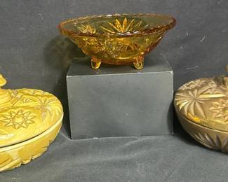 Starburst Lidded Dishes & Amber Glass Bowl Decorative trio featuring two lidded dishes with raised geometric starburst designs and a coordinating amber glass footed bowl. Great for candy, trinkets, or colorful display.  Includes 2 lidded dishes and 1 footed amber glass bowl Raised starburst and geometric designs Finish loss/chipping present on the darker gold-toned lidded dish Please see photos for condition and measurements Market Insight & Estimated Market Value: The bold geometric patterns and warm amber/gold tones give this group a fun vintage-inspired look for display or functional décor.  Estimated Market Value: $25–$45