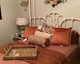 The white cast iron bed with mattress and springs in all her glory with rust colored pillows, straw tray.