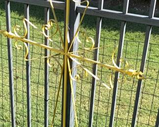 Very large yellow metal cross on fence.
