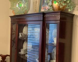 China cabinet with glass platter, behind 2 clear white glass vases with vine, picture,vase with greenery.