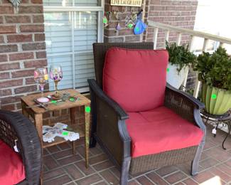2 black wicker chairs with red cushions. Beside them is a hand painted table with hand painted wine glasses.
