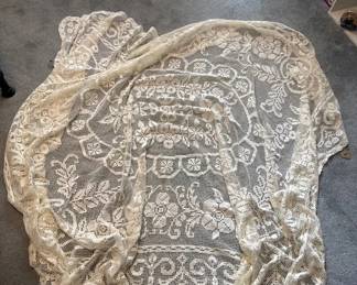 Cream-colored lace shawl or wrap with intricate floral and scrollwork patterns throughout. The delicate lacework appears to be hand-made or fine machine-made lace from the late 19th or early 20th century.