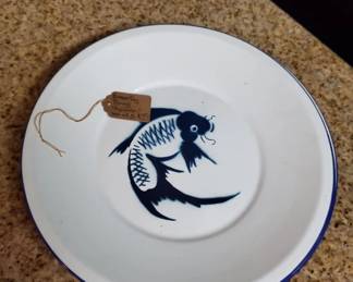 White ceramic plate with a hand-painted blue fish motif in the center. Includes a small wooden tag or label attached with twine.
