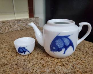 Porcelain teapot and matching teacup decorated with blue fish motifs in an Asian style. The set features a traditional rounded teapot with spout and handle, paired with a small handleless cup.