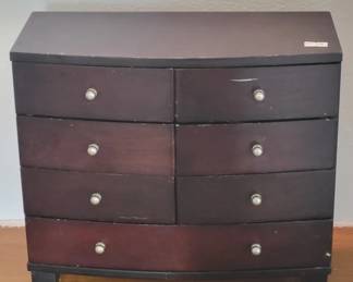 Four-drawer wooden chest with a dark finish and simple round knob hardware. The piece shows visible wear and color variation across the drawers, consistent with age and use.