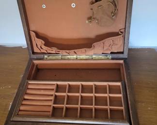 A vintage wooden jewelry box with a hinged lid and divided interior compartments for organizing rings, earrings, and other small items. The box features a tan fabric-lined interior and appears to be in good condition.