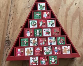 Red wooden advent calendar shaped like a Christmas tree with 24 numbered compartments for holding small gifts or treats. Features festive holiday imagery on the front panels.