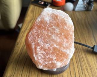 Natural Himalayan salt crystal lamp with a warm glow, mounted on a dark wooden base. Includes electrical cord for ambient lighting.