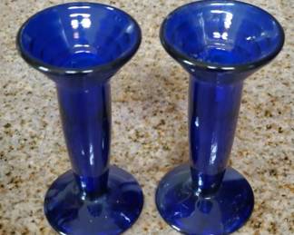 Two matching cobalt blue glass vases with flared rims and cylindrical stems, likely early-to-mid 20th century. Simple, functional design suitable for displaying single flowers or small bouquets.