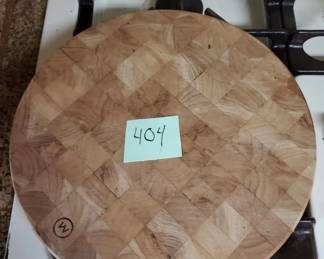 Circular wooden cutting board with a parquet or marquetry pattern on the surface. Shows normal wear and has a small hole near the edge, likely for hanging.