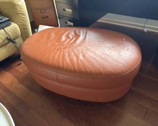 Oval leather ottoman in cognac or tan color with a quilted top surface. Shows some wear and patina consistent with age and use.