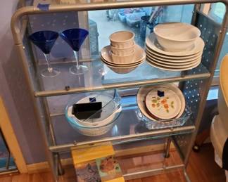 Glass-front display cabinet with wooden frame containing vintage plates, bowls, and serving dishes. The cabinet features two glass shelves and appears to be from the mid-20th century.