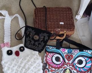Brown wicker suitcase with leather handles, accompanied by a black quilted fabric bag and a colorful patterned pouch with owl design. Also includes a white knitted item and loose buttons.